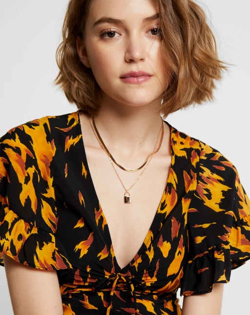 model wearing black patterned top and gold necklaces