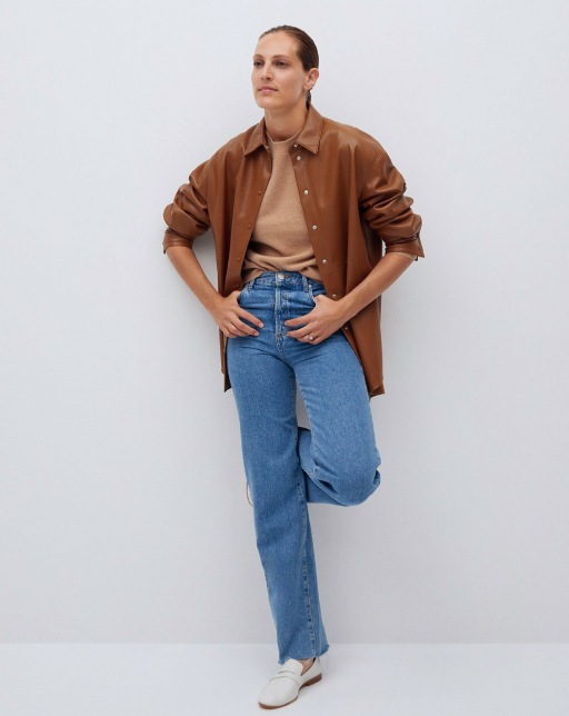 model standing wearing tan sweater topped with button down shirt